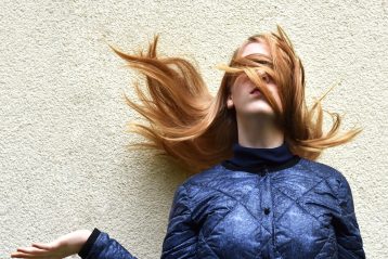 Woman standing against a wall with her hair covering her eyes.