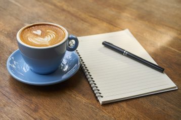 A cup of coffee sitting next to a notebook and pen.
