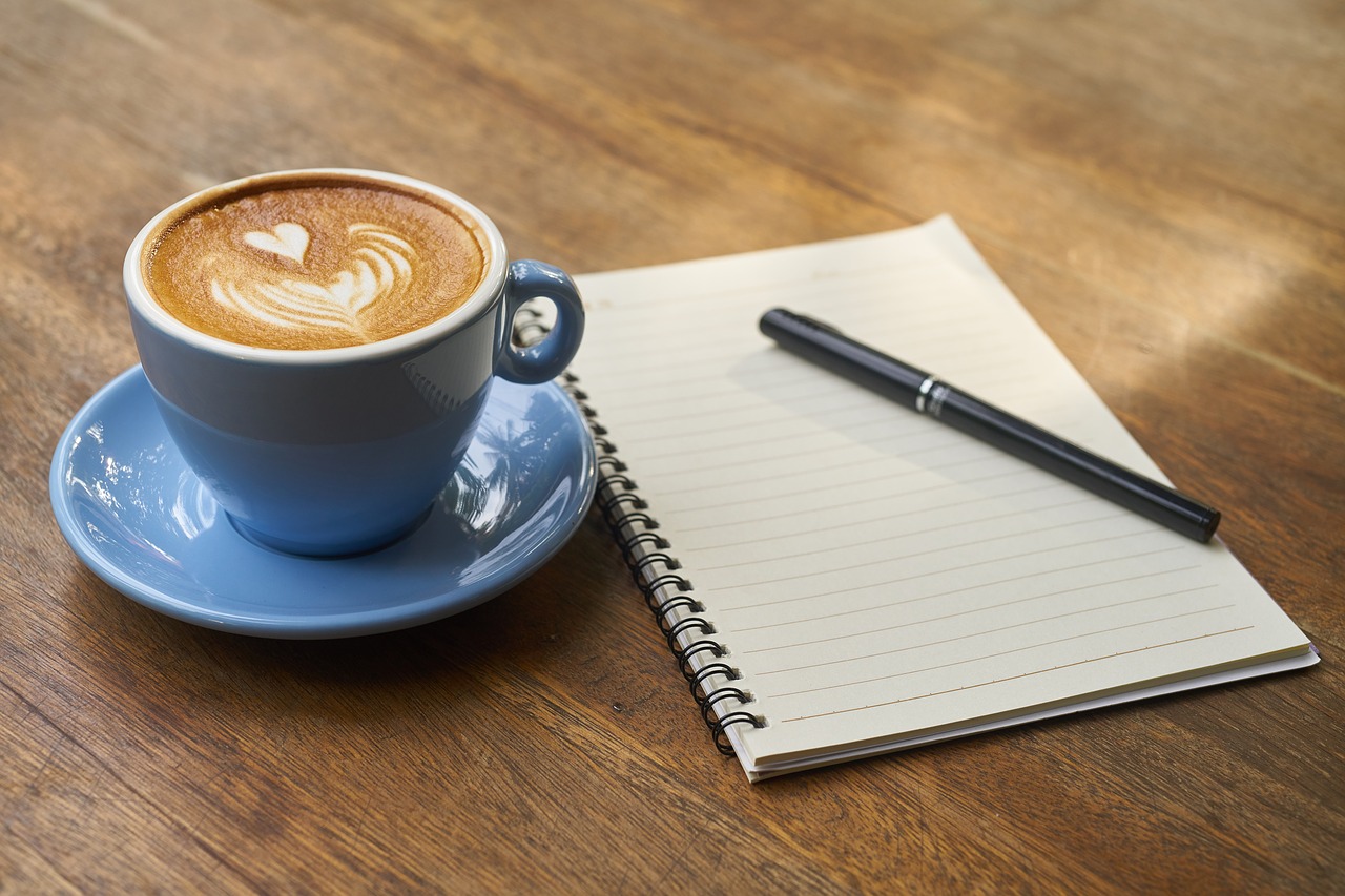 A cup of coffee sitting next to a notebook and pen.