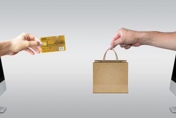 A hand with a credit card reaching out to a hand with a shopping bag.