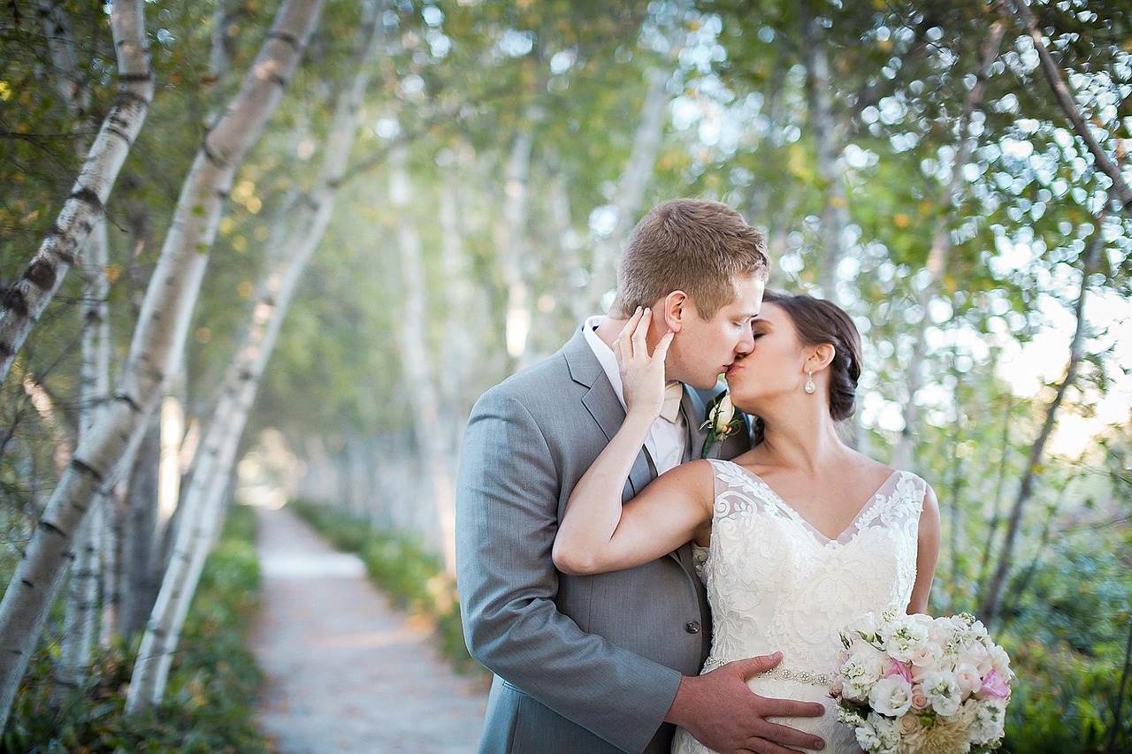Bridal couple kissing outside by a row of trees.