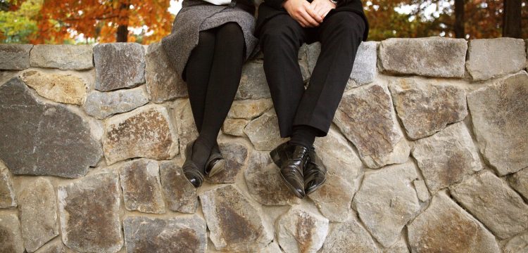 A couple sitting on a stone wall, linking arms.