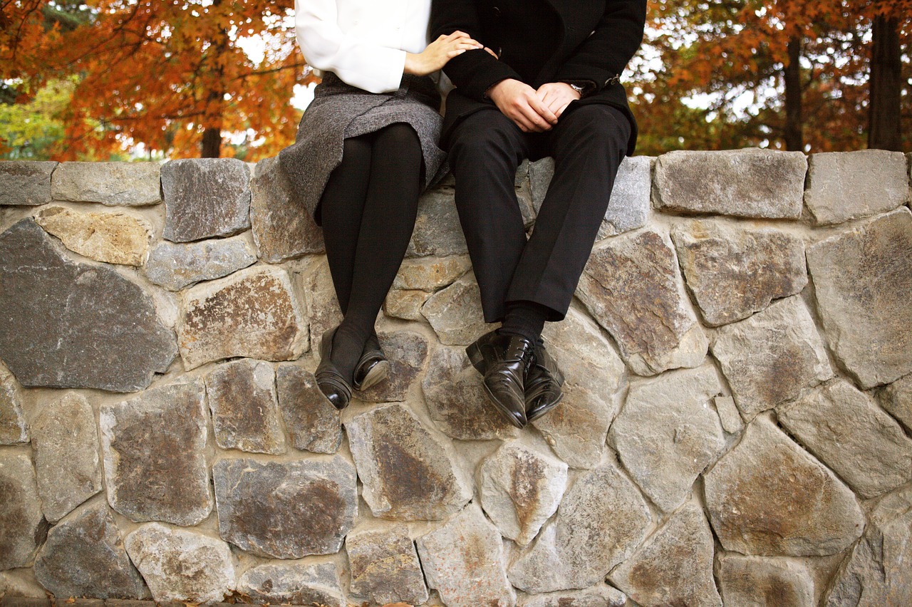 A couple sitting on a stone wall, linking arms.