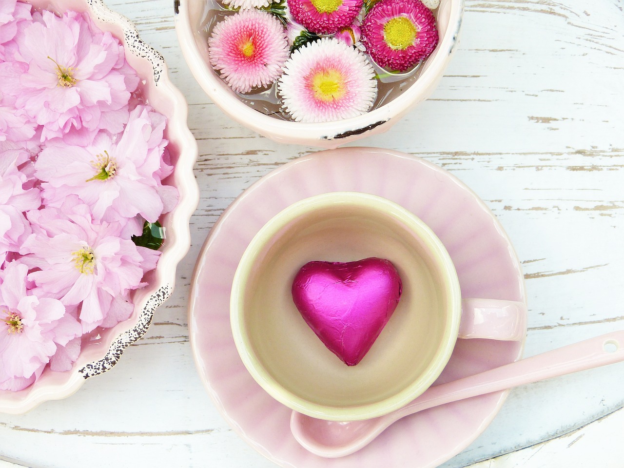 Pink flowers in bowls and a cup on a pink saucer with a pink heart in the center.