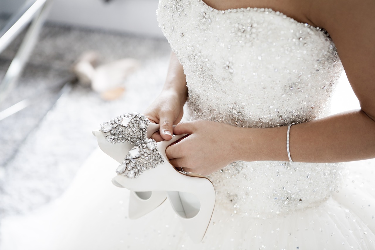 A bride in a beautiful gown, holding wedding shoes.