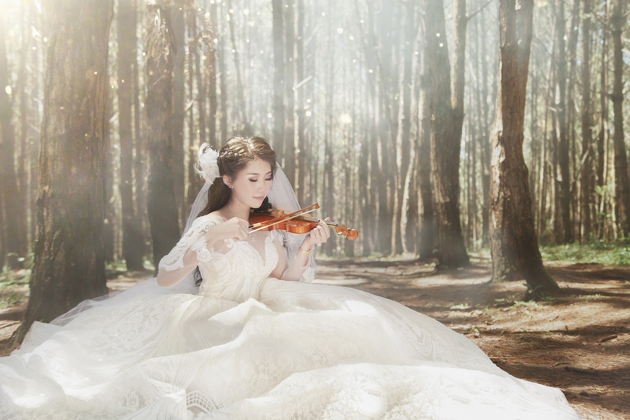 A bride playing a violin in the woods.
