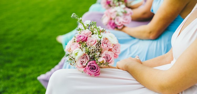 A row of bridesmaids sitting with a bride and with flower bouquets.