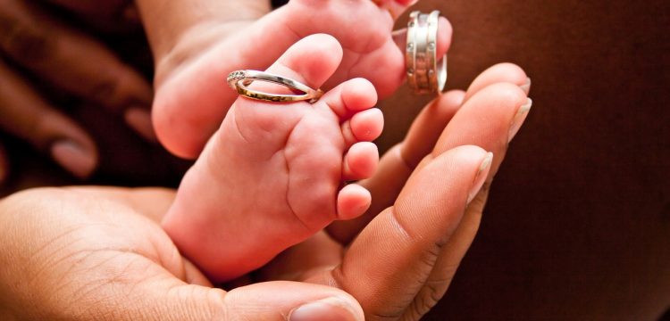Newborn baby's feet with wedding rings on the toes.