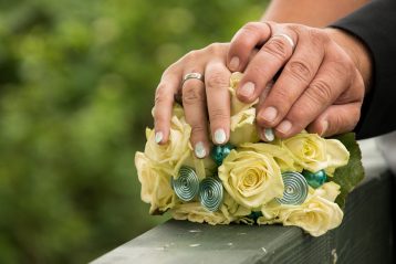 A bride and groom's hands resting on a bridal bouquet.