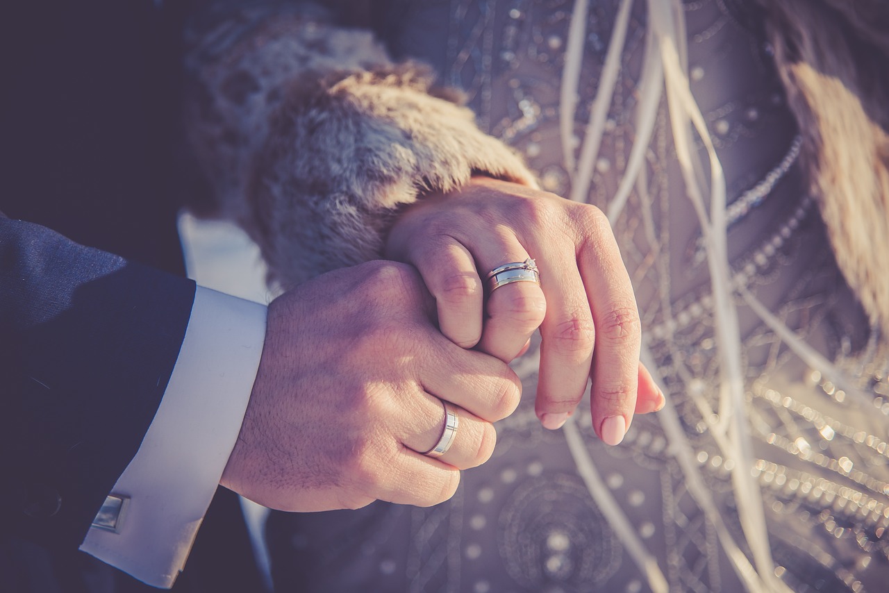 Man and woman wearing wedding rings and holding hands.