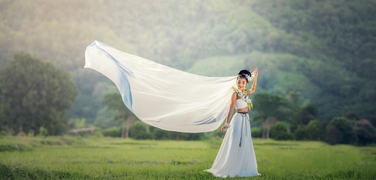 Bride in field with her veil flying in the wind.