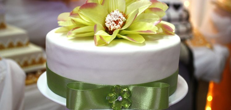 A green and white wedding cake with a large flower on top.