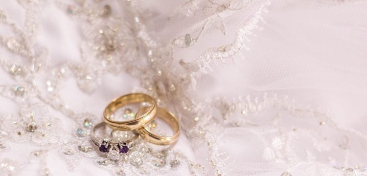 Three wedding rings laying on a wedding gown.