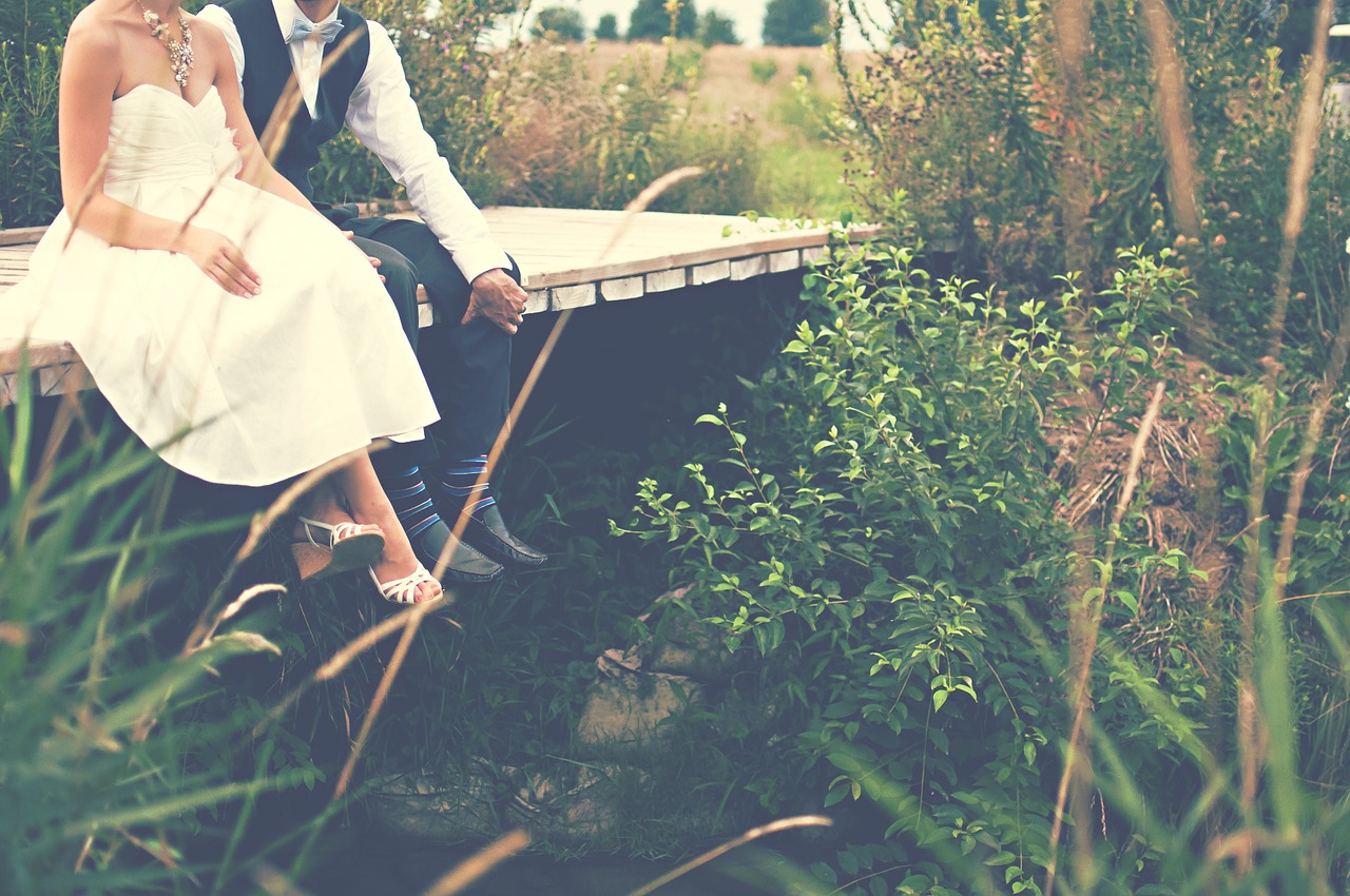 Bride and groom sitting on a small bridge, feet dangling.