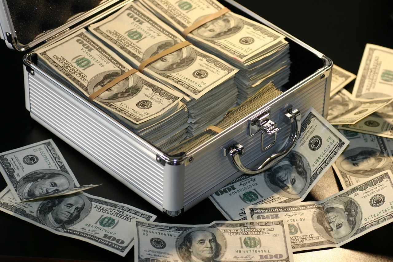 A metal box filled with cash on a table surrounded by more bills.