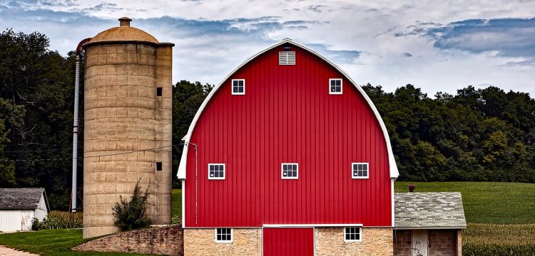 A red barn with a sloped roof next to a silo.