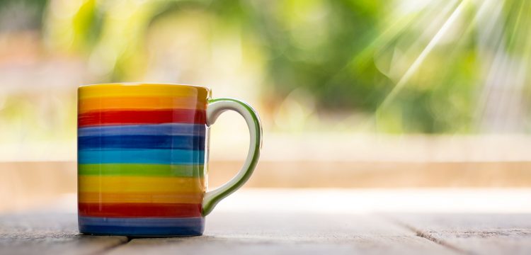 A rainbow mug with the sun shining down on it.