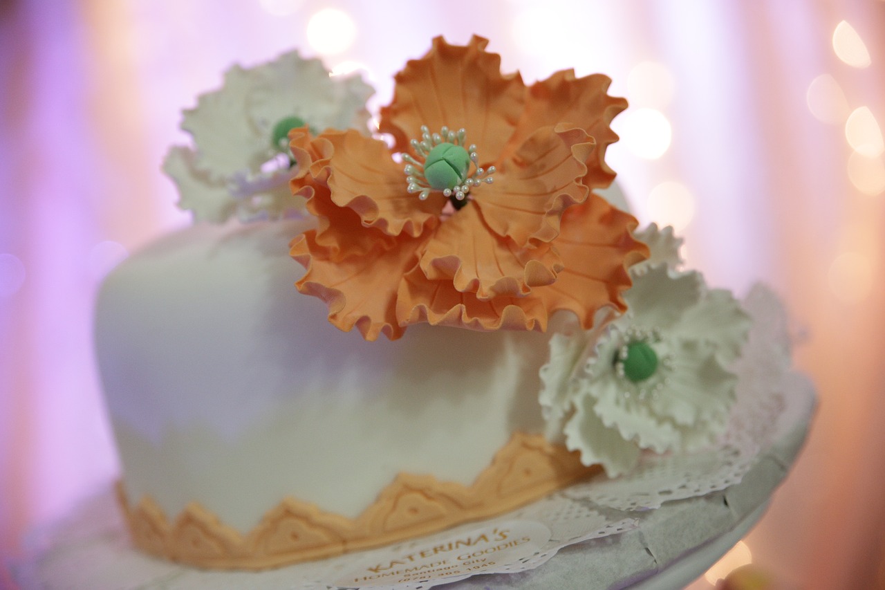 A close up of a wedding cake with a large orange icing flower on it.