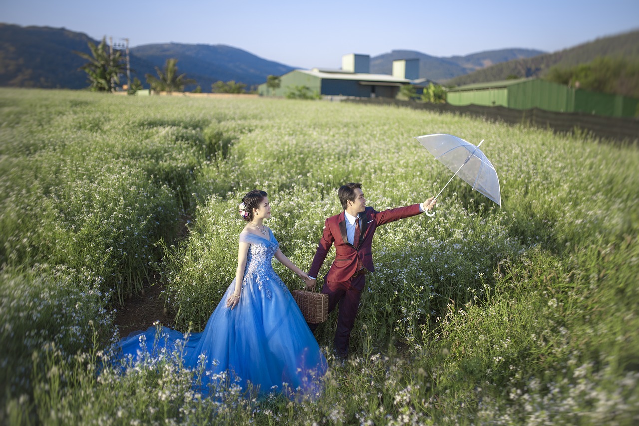 A bride and groom standing in a field with the groom holding an umbrella.
