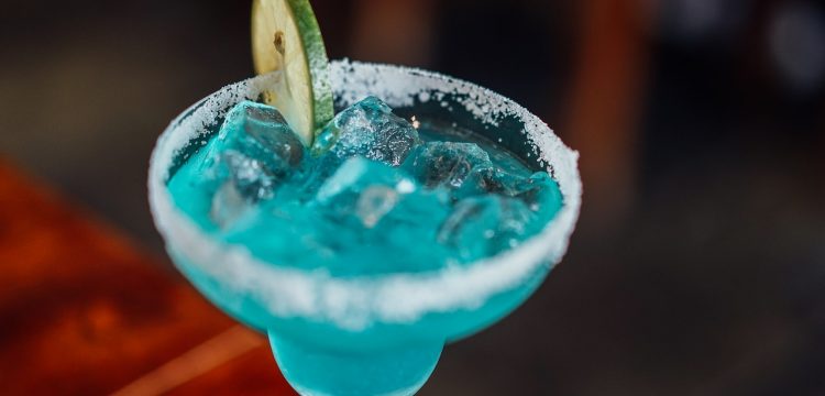 A blue cocktail with a slice of lime in it.