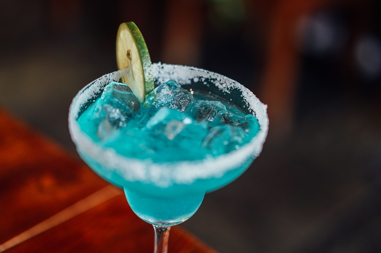 A blue cocktail with a slice of lime in it.