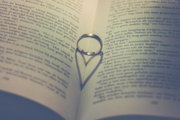 Wedding ring standing upright in a book with its shadow in the shape of a heart.