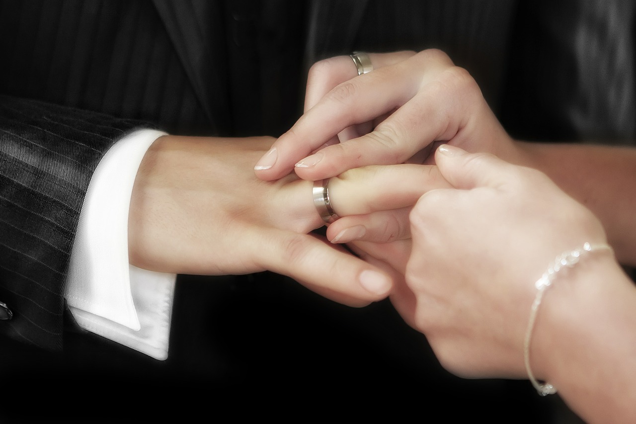 A woman putting a wedding band on a man's hand.