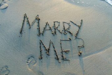 "Marry Me?" written on a beach.