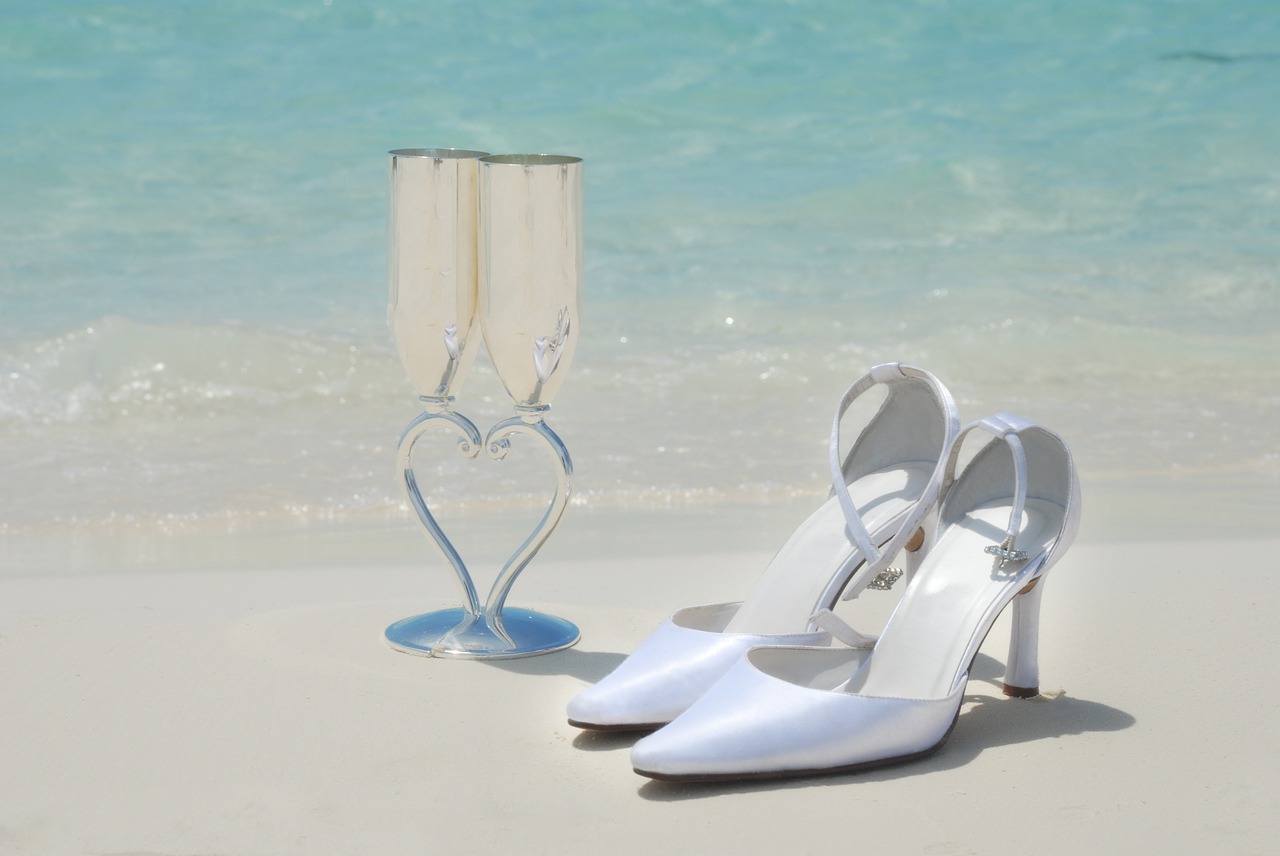 Glasses of champagne and wedding shoes on a beach.
