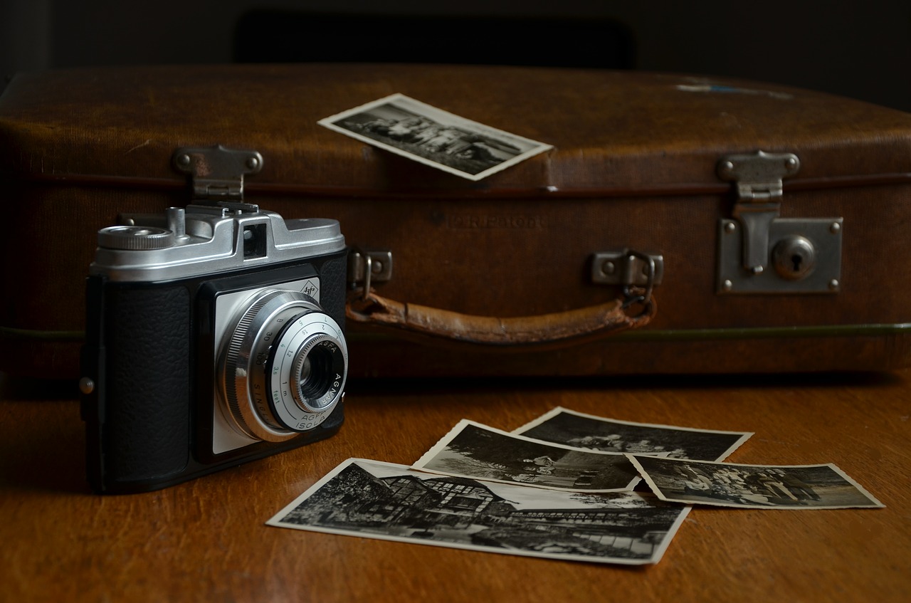 An old camera and suitcase with photos scattered about.