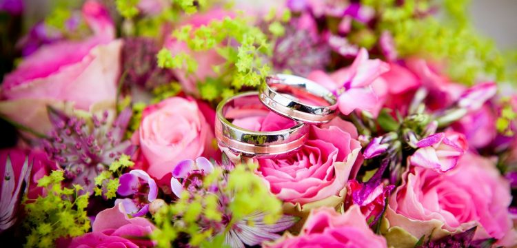 Two wedding bands on top of colorful flowers.