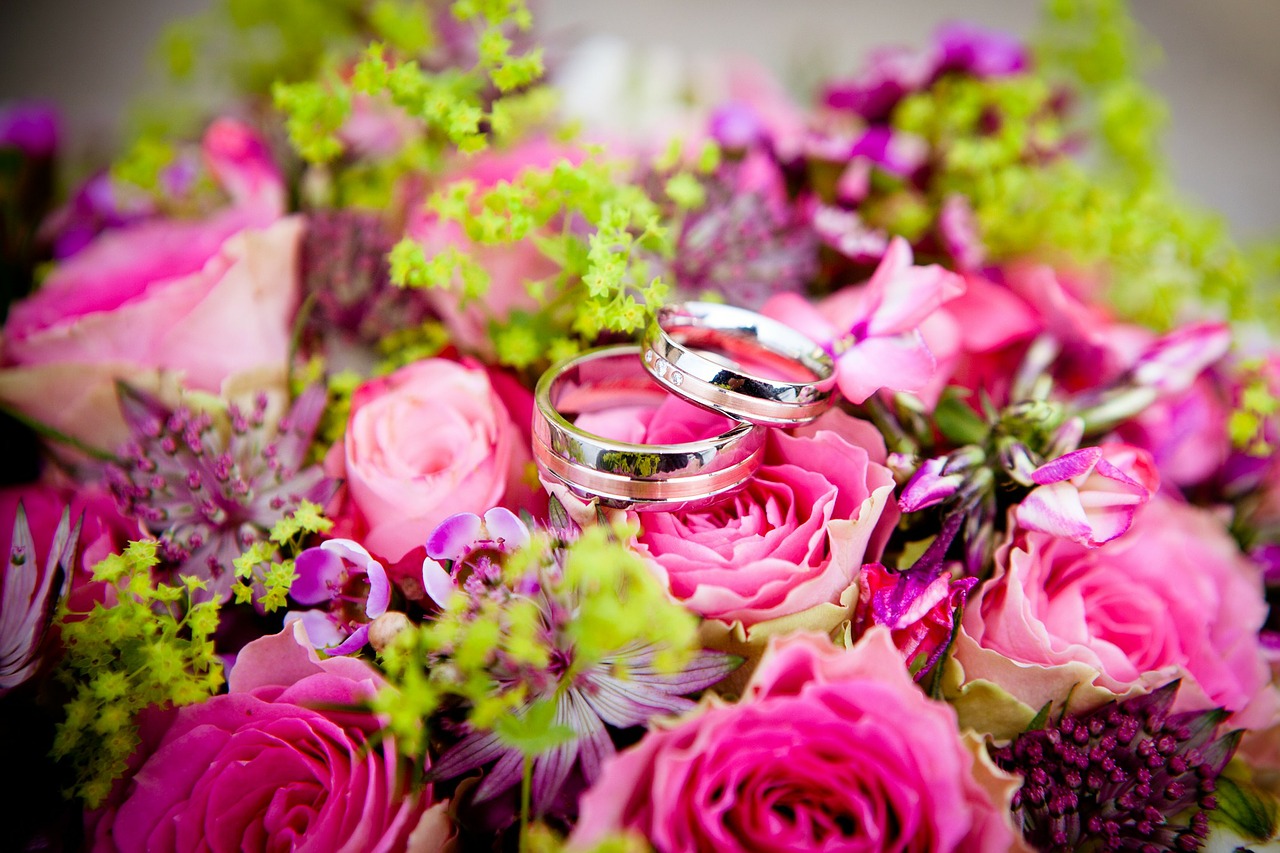 Two wedding bands on top of colorful flowers.