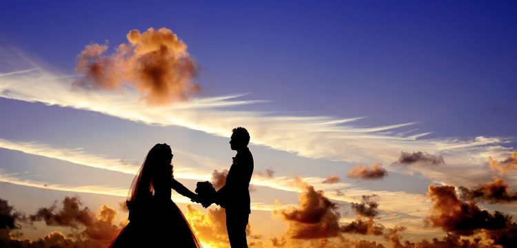 A bridal couple in silhouette in front of a sunset.