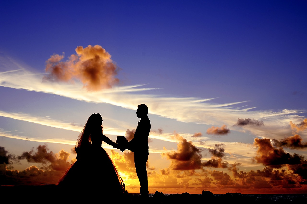 A bridal couple in silhouette in front of a sunset.