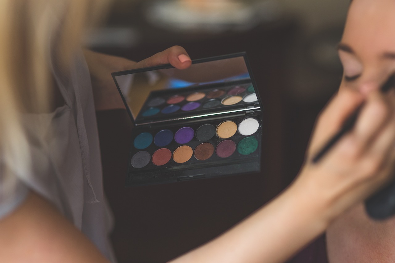 A makeup artist holding an eyeshadow palette and applying the shadow to a woman.