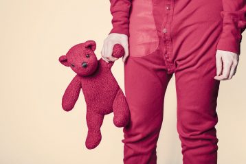 Person in red pajamas holding a red teddy bear.