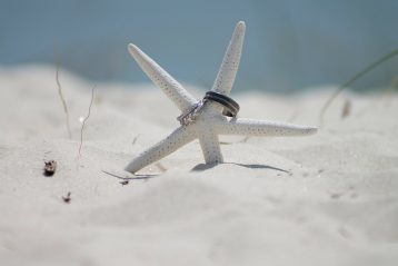 A starfish in the sand with two wedding rings on it.