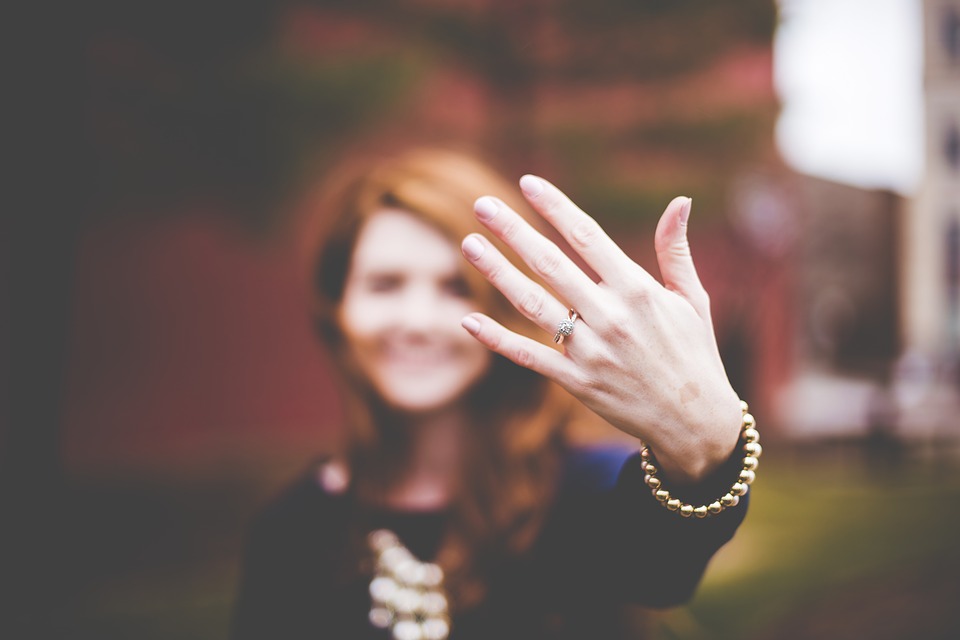 Woman holding up her hand with a diamond ring on it.
