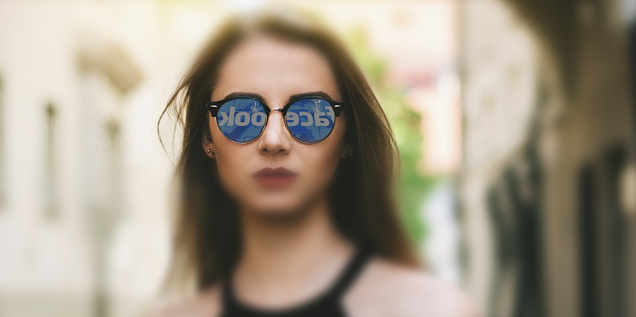 A woman with the Facebook logo reflected in her sun glasses.