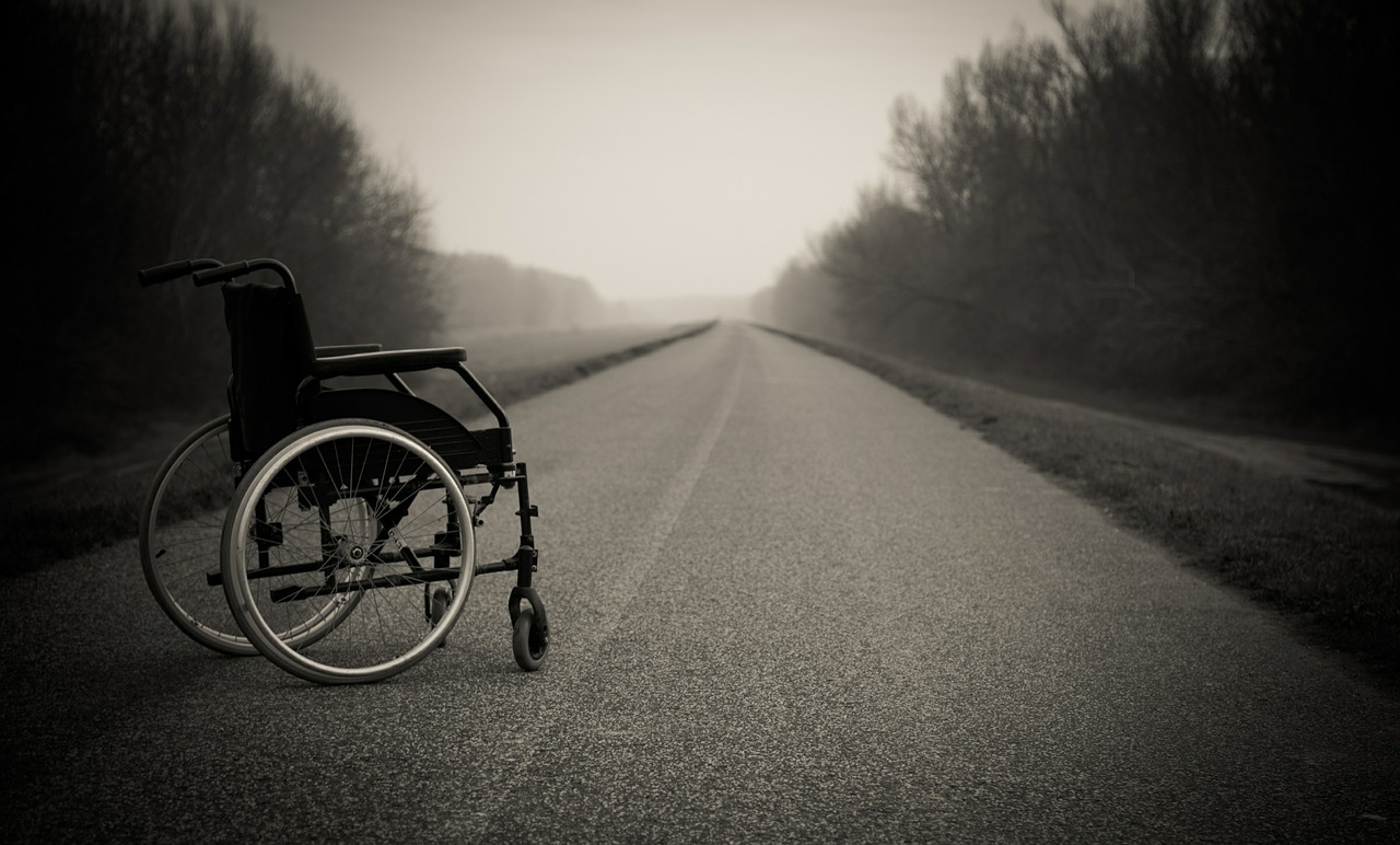 Black and white photo of a wheelchair sitting on an empty road.