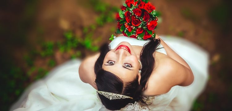A bride holding a bouquet of red flowers looking upwards at the camera.