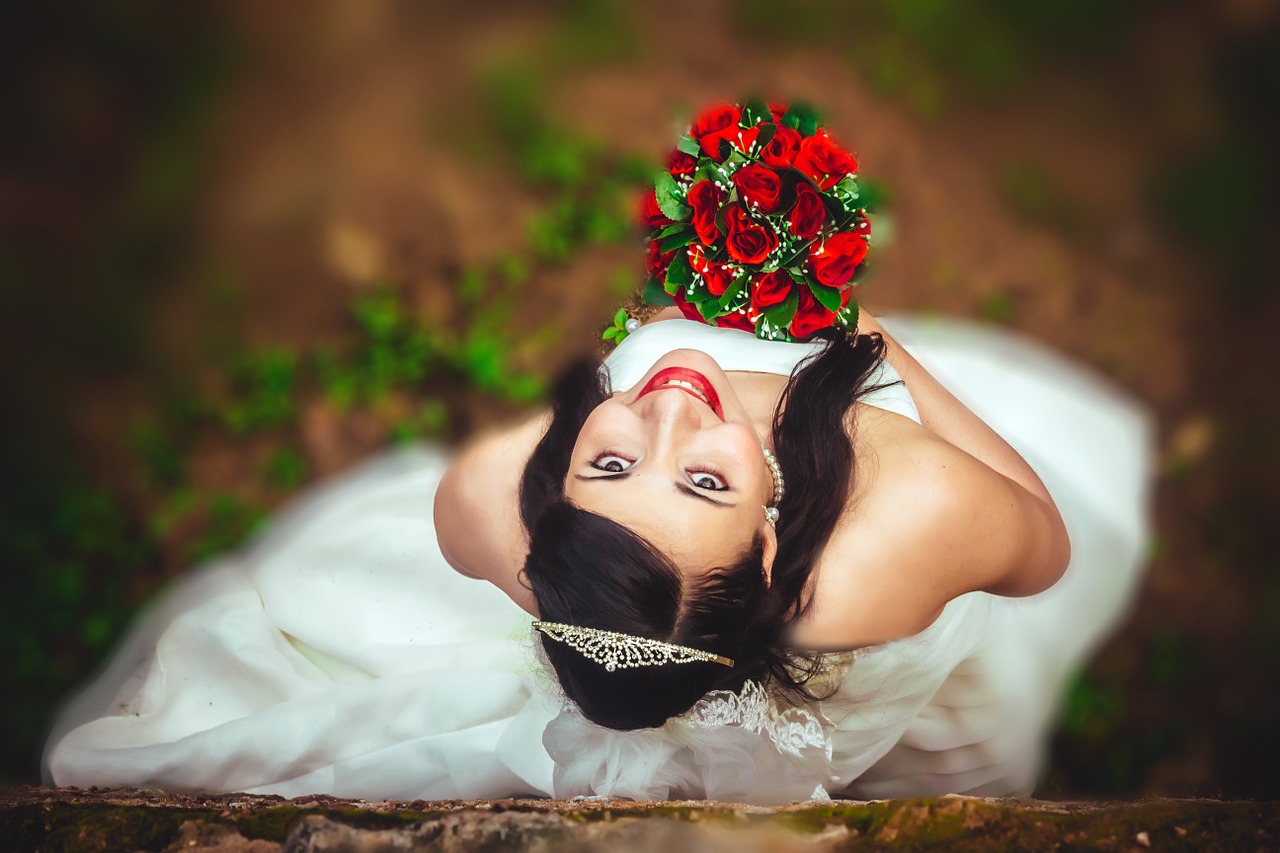 A bride holding a bouquet of red flowers looking upwards at the camera.