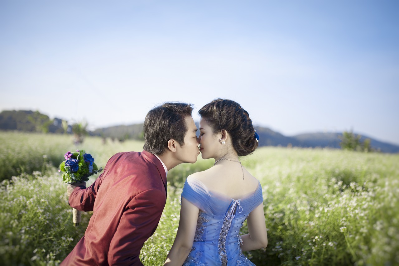 An Asian bride and groom kissing in a beautiful field.