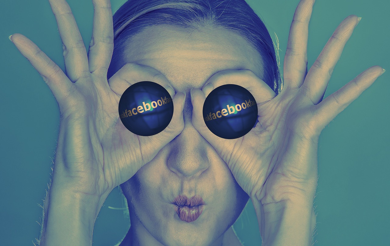Person holding two cylindrical objects in front of her eyes that have the Facebook logo on them.