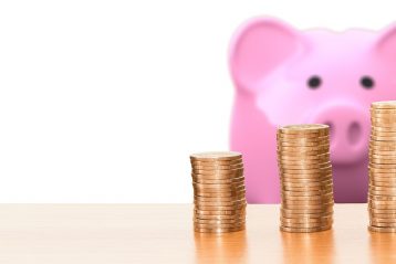 A pink piggy bank with coins in front of it.