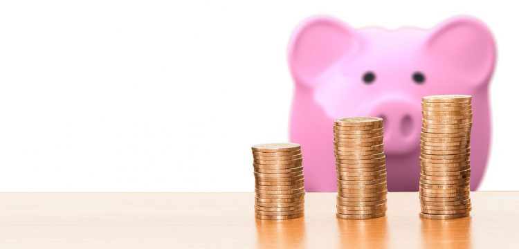 A pink piggy bank with coins in front of it.