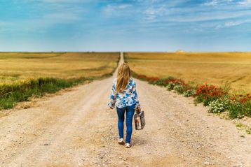 Woman walking down a long road with a suitcase.