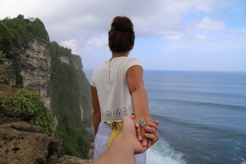 Woman holding a man's hand while standing at the edge of a cliff.