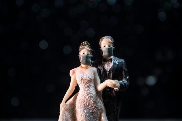 Wedding cake topper with bride and groom wearing masks.