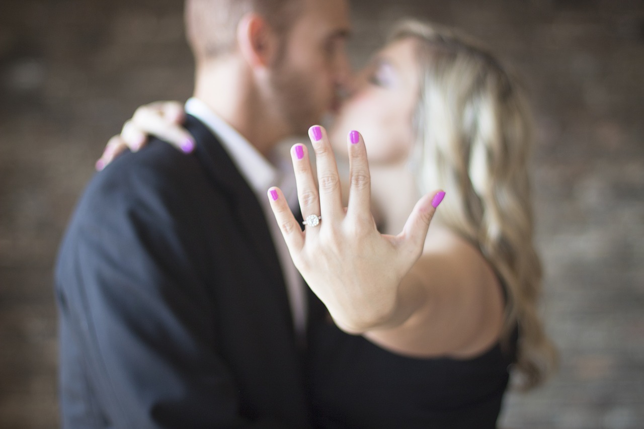 Man and woman kissing, with woman holding out hand with engagement ring on it.